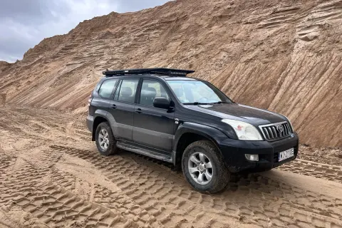 Czarny Land Cruiser 120 na piaszczystym podłożu, z bagażnikiem dachowym, gotowy na terenową przygodę.