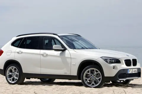 Białe BMW X1 E84 na piaszczystej plaży, z widokiem na morze w tle.