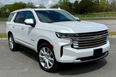 Biały Chevrolet Tahoe z chromowanymi felgami stoi na drodze, otoczony zielenią i chmurami.