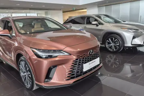 Dwa luksusowe SUV-y Lexus w salonie. Jeden w kolorze miedzianym, drugi srebrny, błyszczą na wypolerowanej podłodze.