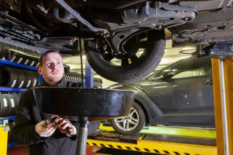 Mechanik wymienia olej w samochodzie, zbierając zużyty płyn do miski.
