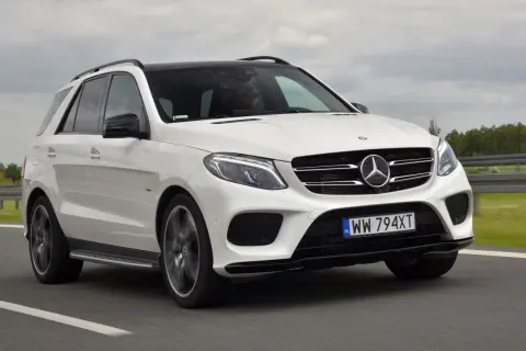 Biały Mercedes GLE 400d z czarnym dachem pędzi po drodze. Kierowca w okularach prowadzi auto.