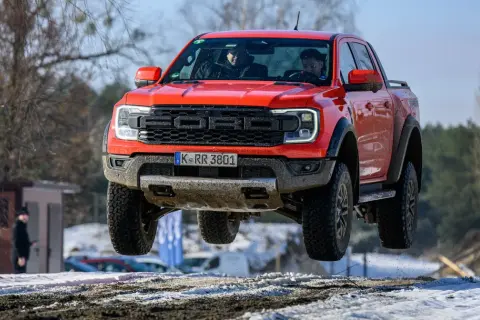 Czerwony Ford Raptor w locie nad śnieżnym terenem. Kierowcy w kabinie, a cena tego potwora budzi podziw.