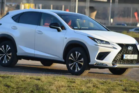 Biały Lexus NX 300 z czerwonym wnętrzem zaparkowany na tle krajobrazu.