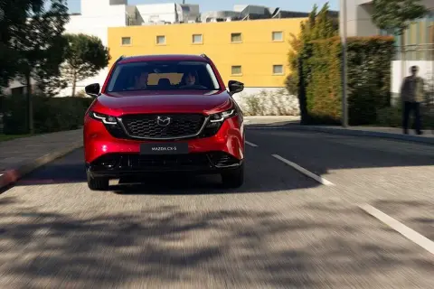 Czerwona Mazda CX-5 jedzie ulicą. W tle budynki i drzewa.