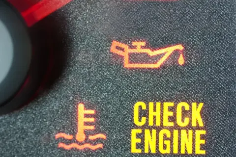 Czerwona kontrolka oleju świeci się na desce rozdzielczej. Obok widać ikonę termometru i napis "CHECK ENGINE".