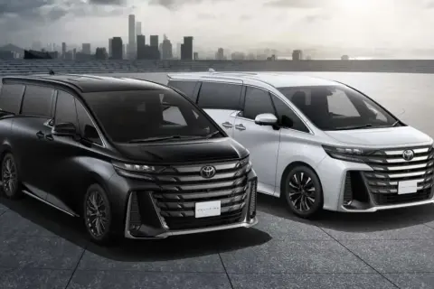 Dwa luksusowe minivany Toyota Vellfire, czarny i biały, prezentują się na tle miejskiej panoramy.