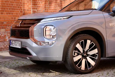 Przód srebrnego Mitsubishi Outlander 2025 z charakterystycznym grillem i reflektorami LED, zaparkowany na bruku przed ceglaną ścianą.