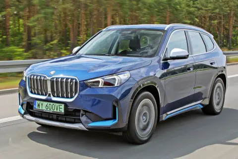 Niebieski BMW X1 elektryk pędzi po drodze wśród drzew.