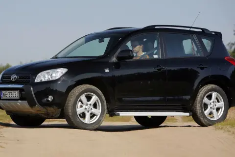 Czarny, mały SUV dla kobiety, zaparkowany na piaszczystej drodze. Kierowca w okularach siedzi za kierownicą.