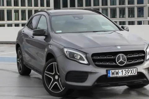 Szary Mercedes GLA 220 z polskimi tablicami rejestracyjnymi stoi na parkingu przed nowoczesnym budynkiem.