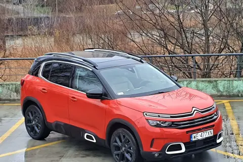 Pomarańczowy Citroen C5 Aircross z czarnym dachem stoi na mokrym parkingu.