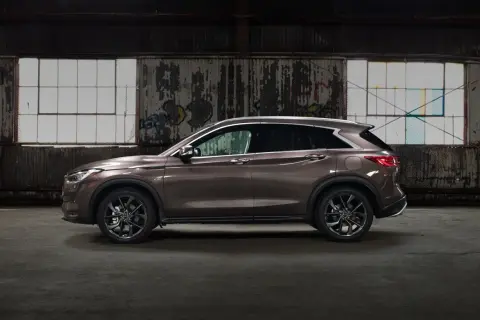 Brązowy Infiniti QX50 w profilu, zaparkowany w opuszczonym magazynie z graffiti na ścianach i dużymi oknami.