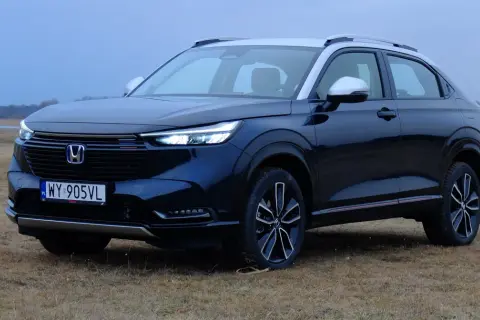 Ciemnogranatowa honda hybryda z srebrnym dachem i lusterkami, zaparkowana na trawiastym polu.