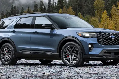 Niebieski Ford Explorer ST na kamienistej plaży, z jesiennym lasem w tle.