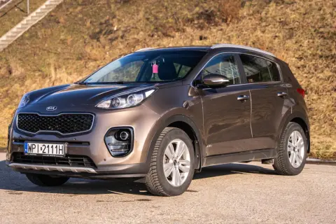 Brązowy Kia Sportage 2017 zaparkowany na tle suchej trawy i schodów.