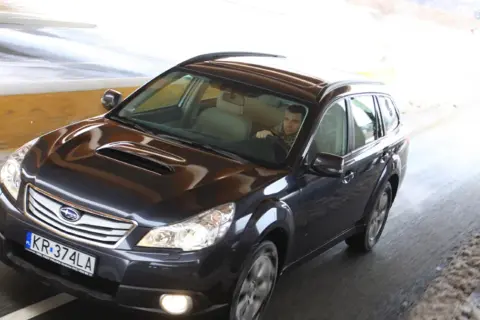 Ciemny Subaru Outback 2025 jedzie przez tunel, kierowca w szaliku.