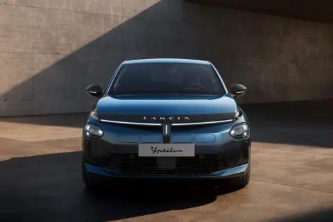 Elegancki, niebieski Lancia Ypsilon 2024 z nowoczesnym przodem, prezentowany na tle betonowej ściany.