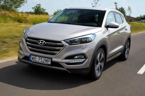 Srebrny Hyundai Tucson 3 jedzie po drodze, otoczony zielenią.
