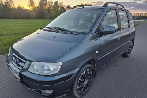 Szary Hyundai Matrix na tle zachodzącego słońca i zielonej łąki.