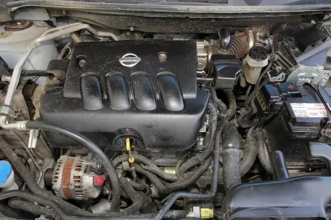 Silnik Nissan Qashqai J10, widok z góry. Czarna pokrywa silnika z logo Nissan, alternator, akumulator i przewody.