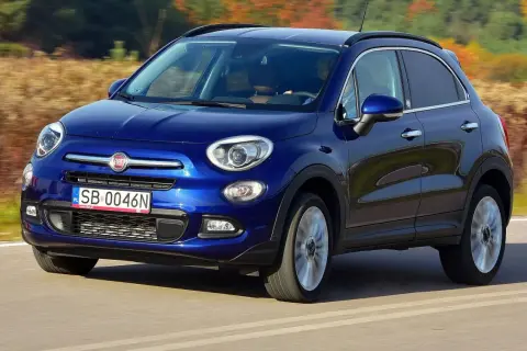 Błękitny Fiat 500X jedzie po drodze, otoczony jesienną przyrodą.