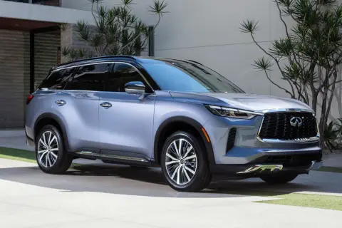 Elegancki, srebrny Infiniti QX60 parkuje przed nowoczesnym domem, otoczony bujną zielenią.
