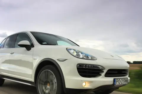 Biały Porsche Cayenne Turbo pędzi po drodze, chmury na niebie sugerują zmienną pogodę.