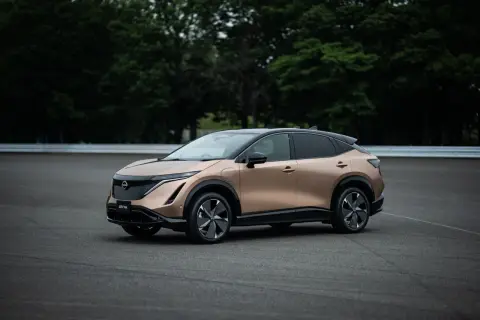 Elegancki, brązowy Nissan Ariya na tle zielonych drzew i asfaltu.