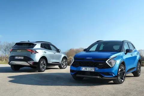Dwa Kia Sportage GT Line: jeden niebieski z przodu, drugi srebrny z tyłu, na tle błękitnego nieba i drzew.