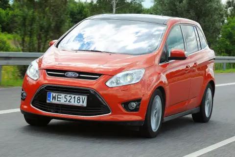 Pomarańczowy Ford C-Max 1.6 benzyna jedzie po drodze, odbijając chmury w szybie.