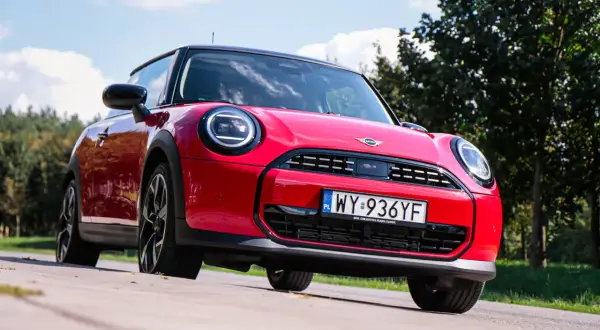 Czerwony Mini Cooper na tle zieleni. Wiele osób szuka opinii o tym modelu, a ten egzemplarz wygląda na gotowy do jazdy.