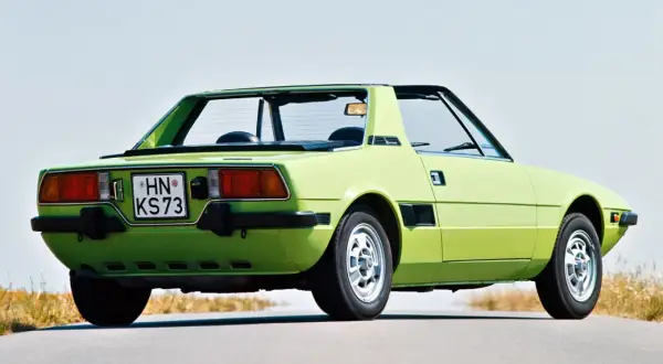 Jasnozielony Fiat X1/9 z lat 70. na pustej drodze, z widokiem na tył i bok.