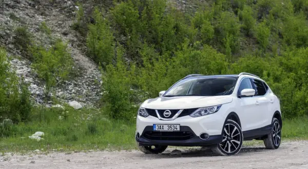 Biały Nissan Qashqai J11 na drodze szutrowej, otoczony zielenią i kamienistym zboczem.