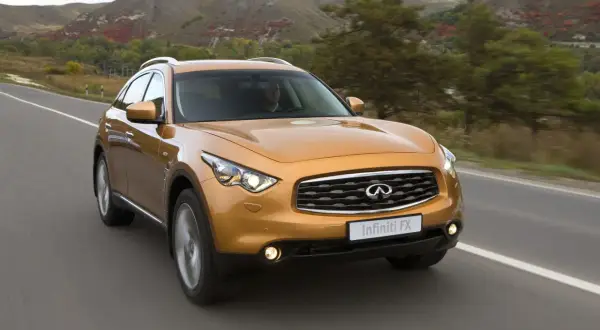 Pomarańczowy Infiniti QX70 jedzie po drodze wśród jesiennych wzgórz.