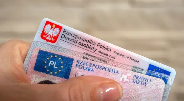 Dłoń trzyma polski dowód osobisty i prawo jazdy. To ważne dokumenty, które pozwalają na legalne poruszanie się po drogach, a niektóre z nich, jak prawo jazdy bezterminowe, są ważne przez całe życie.