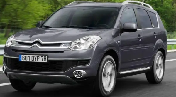 Szary Citroen C-Crosser jedzie po drodze, otoczony zielenią.