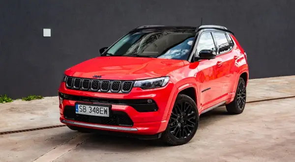 Czerwony Jeep Compass z czarnym dachem i felgami. Zbliżenie na przód auta, gdzie widoczne są charakterystyczne siedmioszczelinowe wloty powietrza. Idealny do miasta i na wyprawy, jego wymiary są dopasowane do potrzeb kierowców.