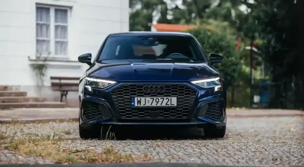 Granatowy Audi A3, segment c, z charakterystycznym grillem i ostrymi światłami, zaparkowany na brukowanej drodze.