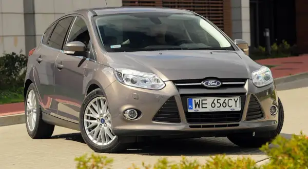 Brązowy Ford Focus 2014, zaparkowany przed nowoczesnym budynkiem, gotowy do podróży.