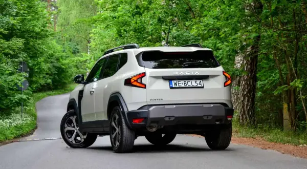 Nowy Dacia Duster 3 na krętej leśnej drodze. Nowoczesne światła i masywna sylwetka podkreślają jego terenowy charakter.