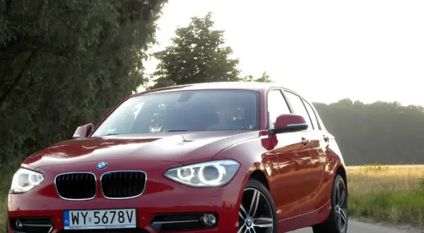 Czerwone BMW 118d na tle drzew i pól.
