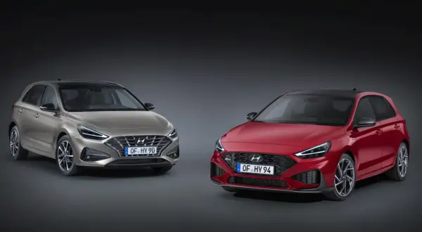 Dwa modele Hyundai i30 2024: jeden w kolorze złotym, drugi w czerwonym, prezentują nowoczesny design i sportowe linie.