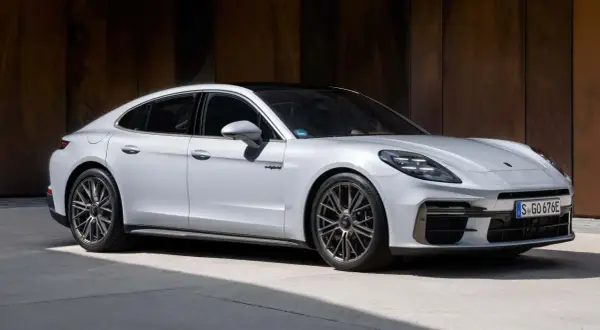Elegancki, biały Porsche Panamera 2024 z czarnym dachem i przyciemnianymi szybami, zaparkowany na tle rustykalnej ściany.