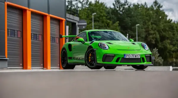 Jaskrawozielony Porsche 911 GT3 RS z czarnym spojlerem i felgami, gotowy do wyjazdu z garażu.