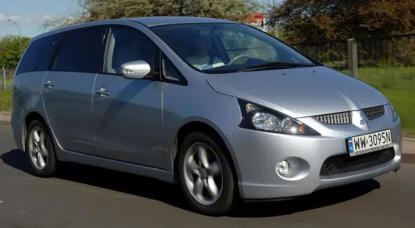 Srebrny Mitsubishi Grandis jedzie po drodze. Kierowca w jasnej koszulce prowadzi auto.