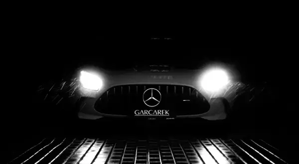 Czarny Mercedes-AMG GT Black Series z włączonymi światłami, stojący na mokrej, metalowej kratce.