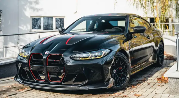 Czarny BMW M4 CSL z czerwonymi akcentami na masce i grillu, zaparkowany na brukowanej nawierzchni.