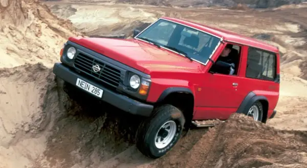Czerwony Nissan Patrol Y60 pokonuje piaszczyste wzniesienie, demonstrując swoje terenowe możliwości.