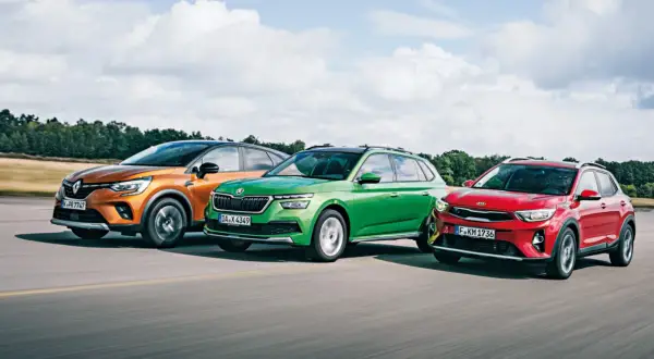 Trzy miejskie crossovery: pomarańczowy Renault, zielona Skoda i czerwony Kia Stonic 2024 jadą po drodze.